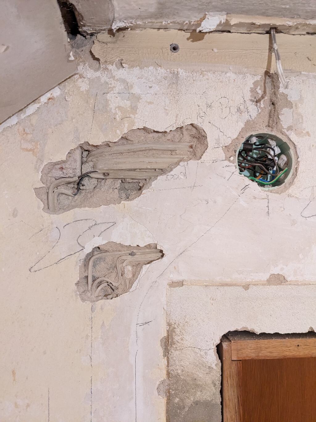 Beschädigte Wand mit offenem Putz, sichtbare Verkabelung und Rohre.