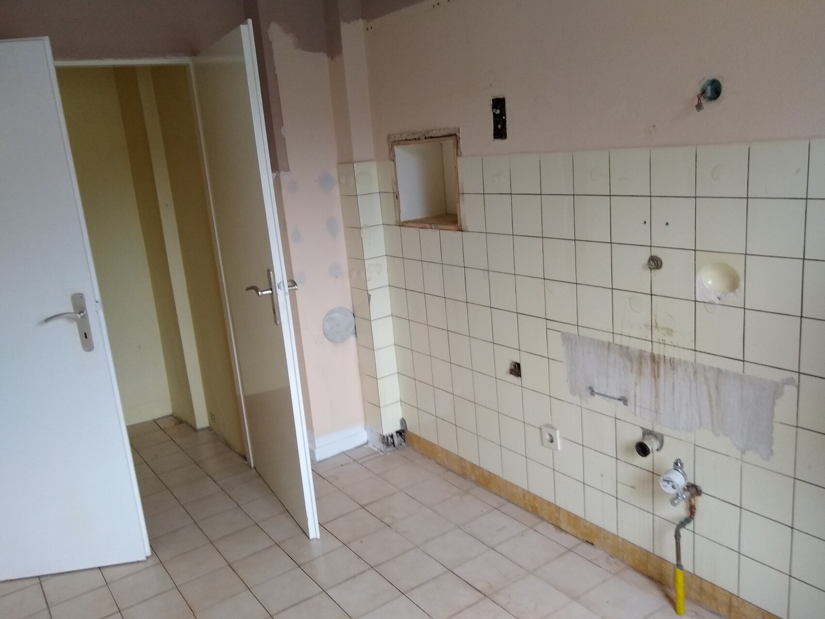 Leere Küche/Waschküche mit Fliesenwand, offenem Wandausschnitt und sichtbaren Rohren