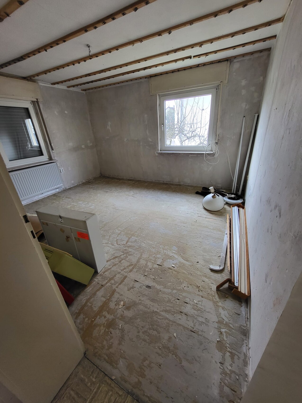 Unrenovierter Raum mit freiliegenden Deckenbalken, rauen Wänden, Baumaterial und Fenster.