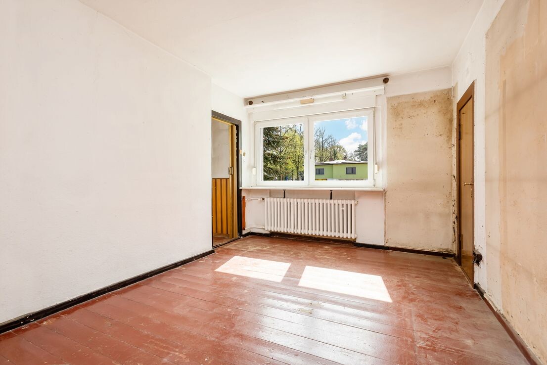 Heller Raum mit Fenster, Heizkoerper und rohem Holzboden in Renovierungsphase