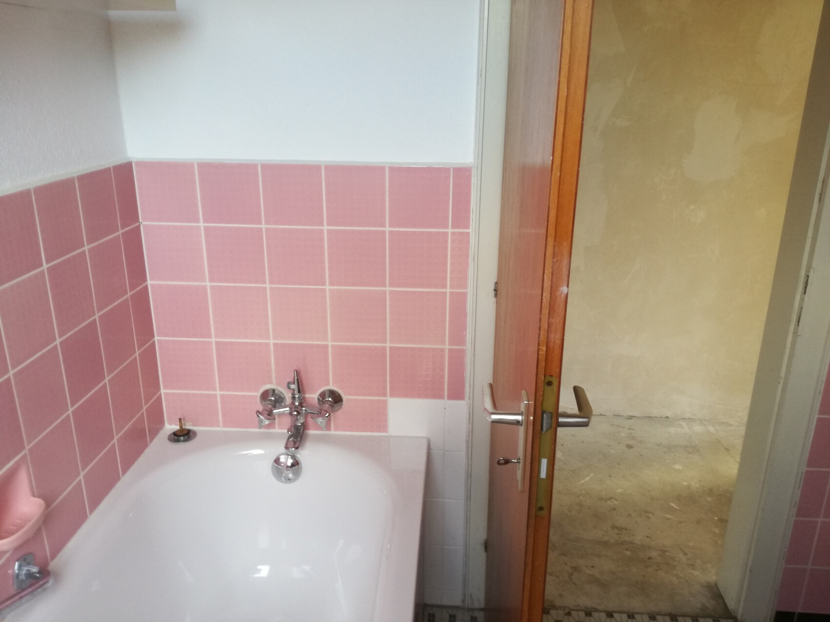 Badezimmer mit rosa Fliesen, weiße Badewanne und geöffnete Holztür zum Flur.