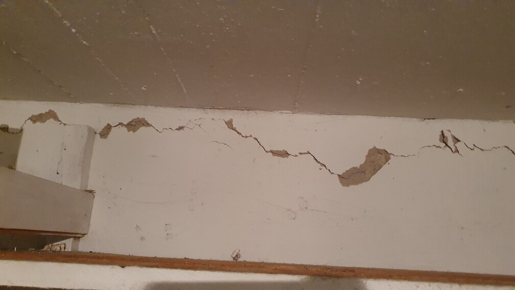 Wandverputz mit Rissen und Abplatzungen, links sichtbares Holzelement.