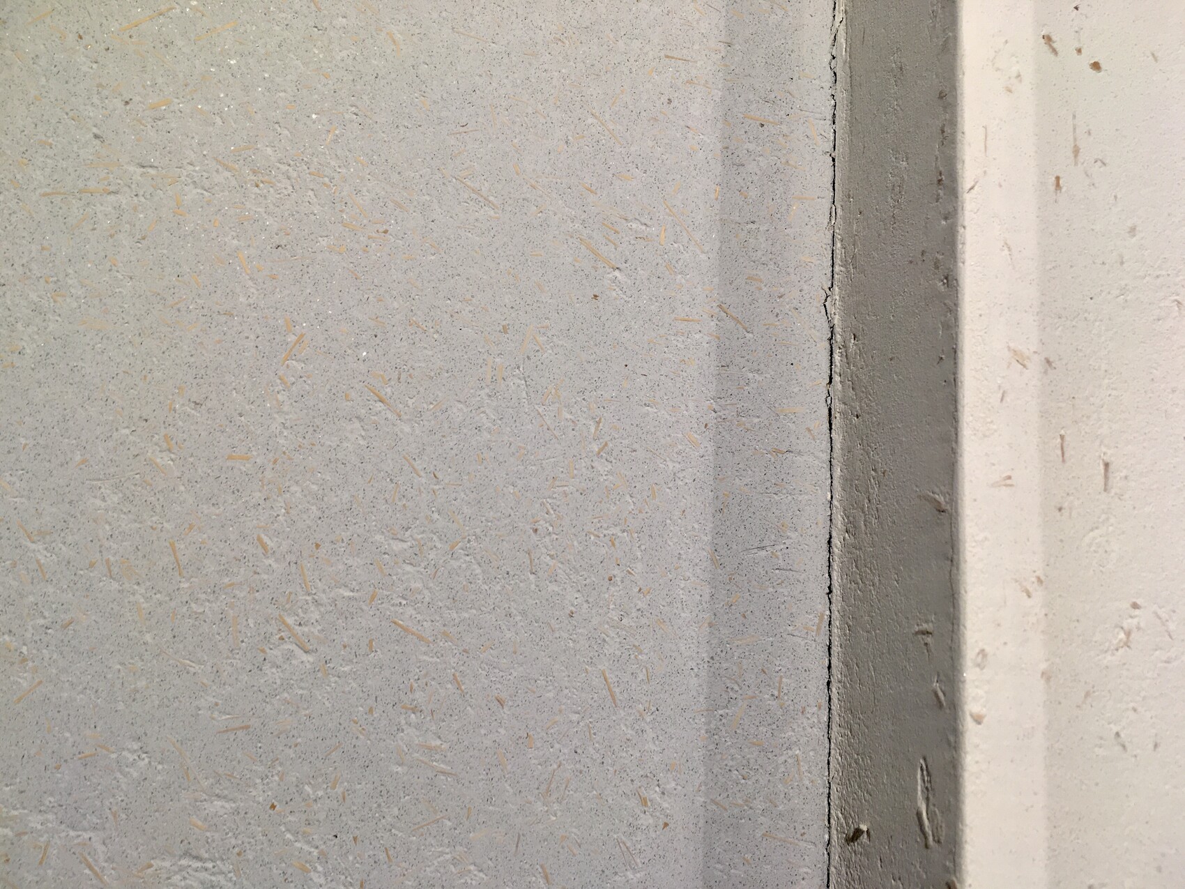 Nahaufnahme einer grauen Wandfläche mit verstreuten orangefarbenen Holzspänen; rechter Rand mit Spalt.