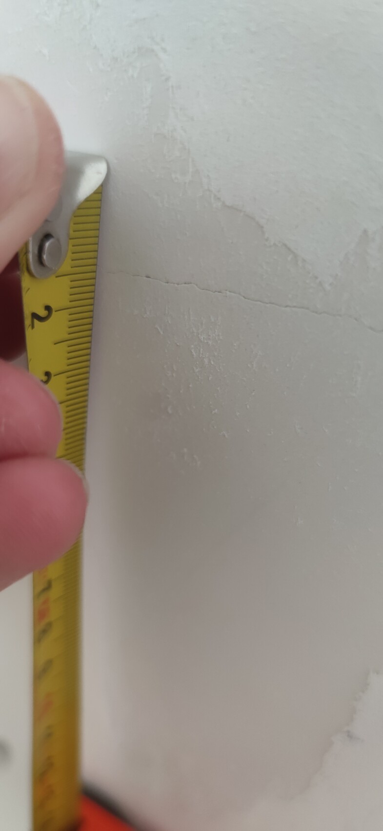 Hand hält gelbes Maßband an einer rissigen weißen Wand