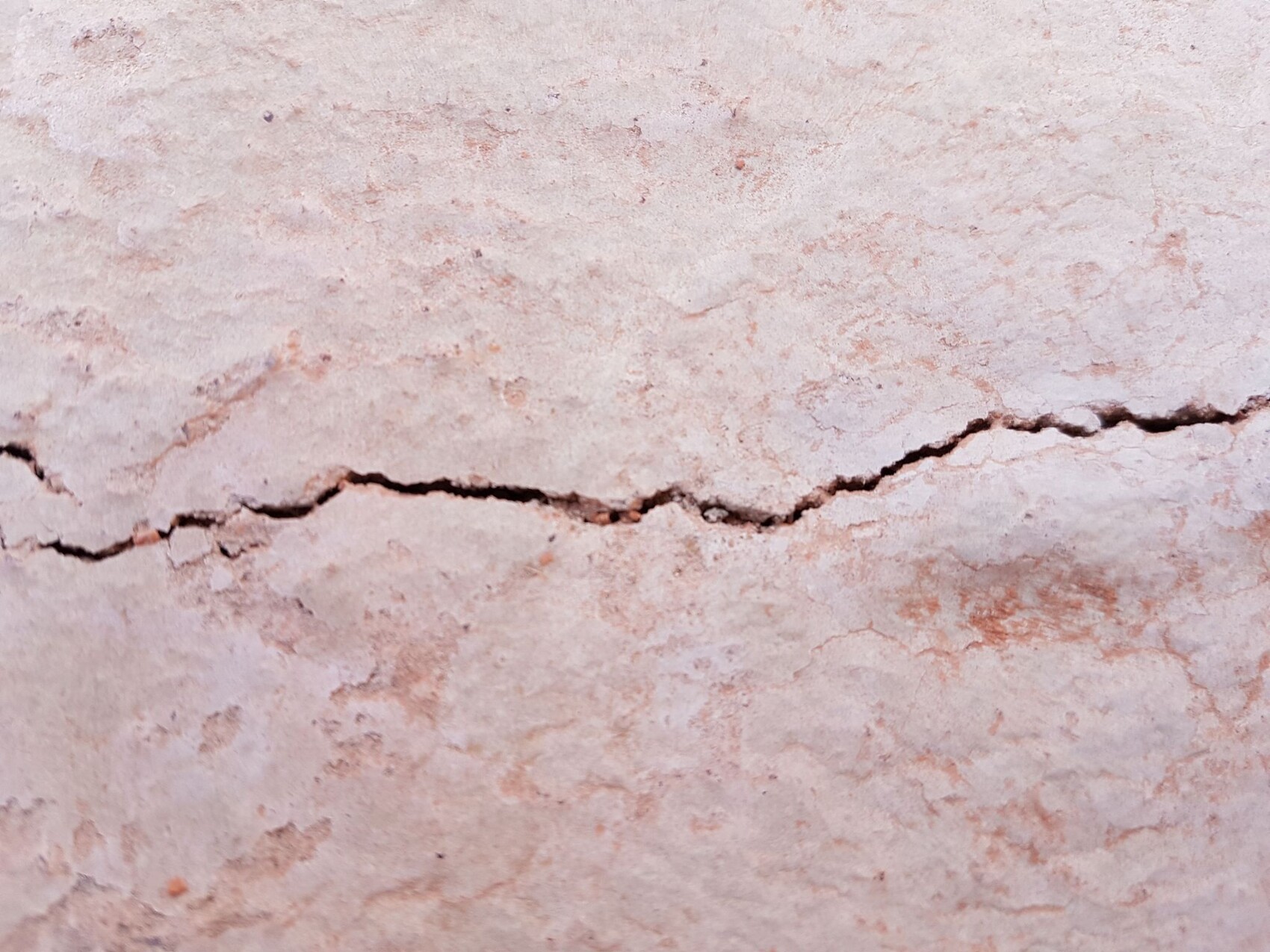 Nahaufnahme einer rissigen Wandputzoberflaeche mit horizontalem Riss