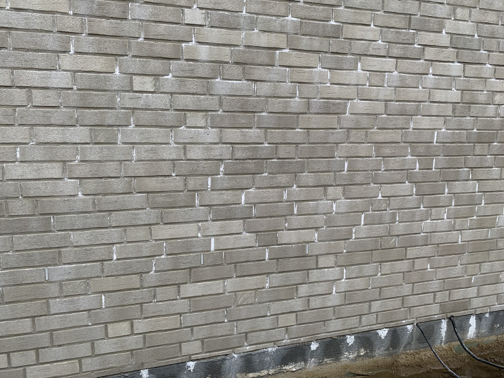 Außenwand aus hellbeigen Ziegeln mit weißem Mörtel, Bodenbereich mit Kabeln sichtbar.