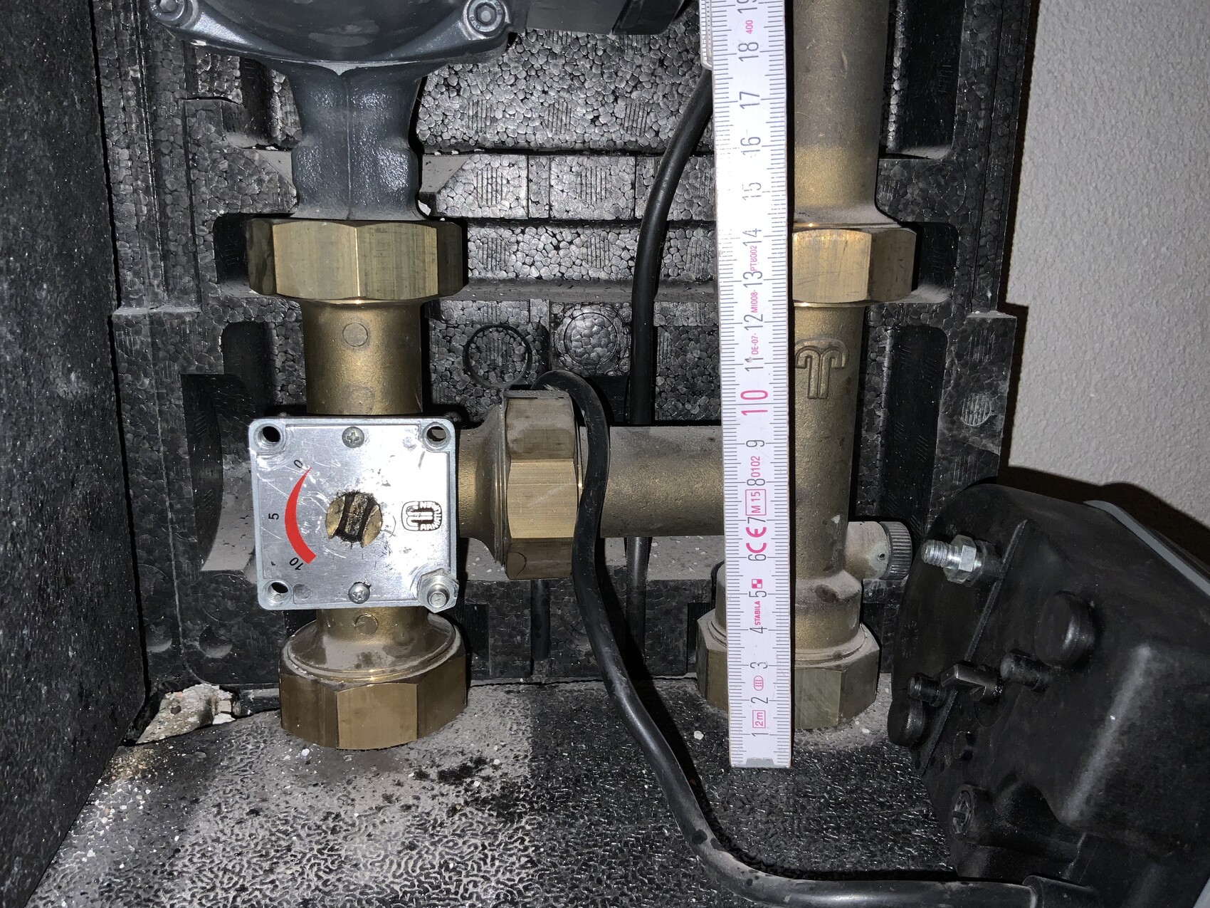 Zwei Messingventile mit Einstellregler in einer Heizungsanlage; daneben ein vertikal platziertes Maßband.