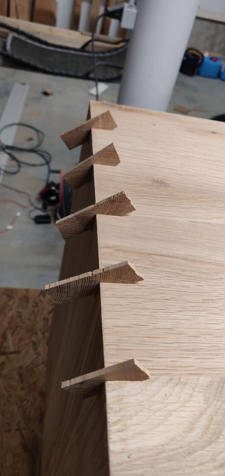 Nahaufnahme eines Holzbretts mit Finger-Verbindungen an der Kante, Werkstatt im Hintergrund.