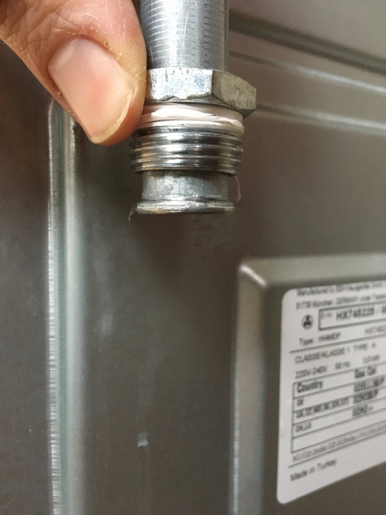 Hand an einer verschraubten Metall-Gewindeverbindung, Dichtpaste am Gewinde sichtbar.