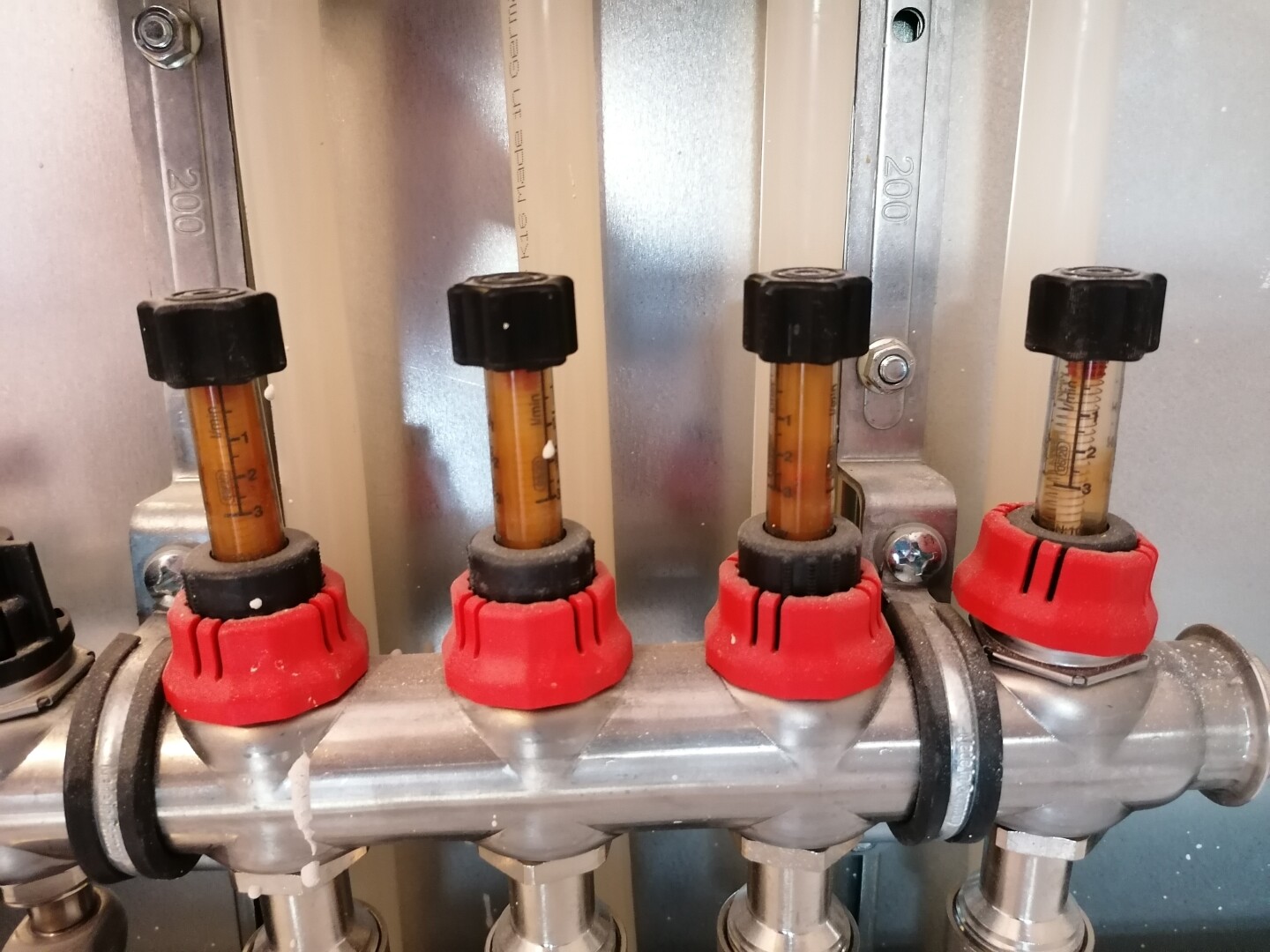 Vier vertikale Glasröhrchen mit orangefarbener Flüssigkeit, rote Kappen an Metallrohrsystem