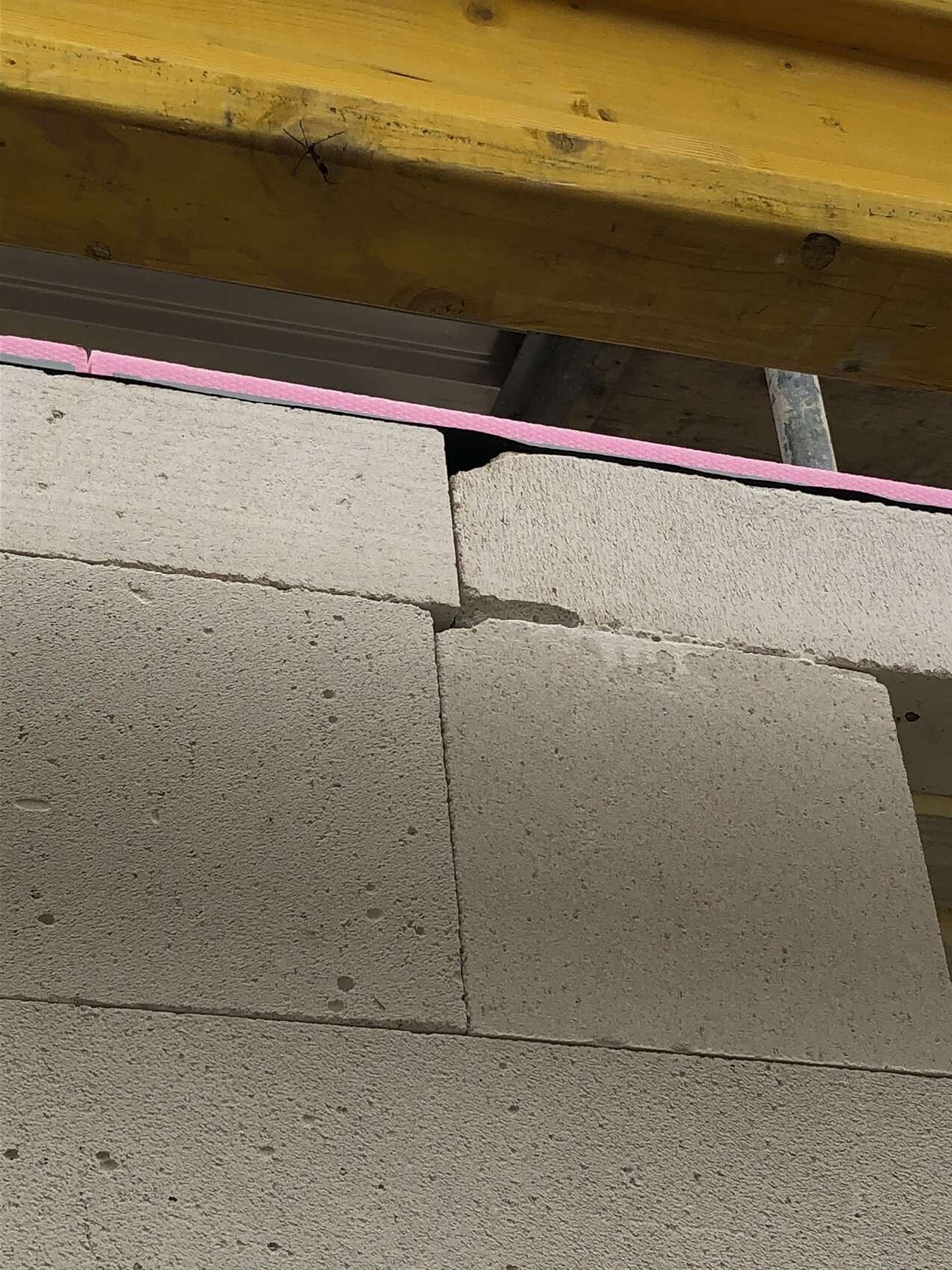 Bauwand aus groben Betonblöcken mit rosa Dämmstreifen und gelben Holzbalken oben.