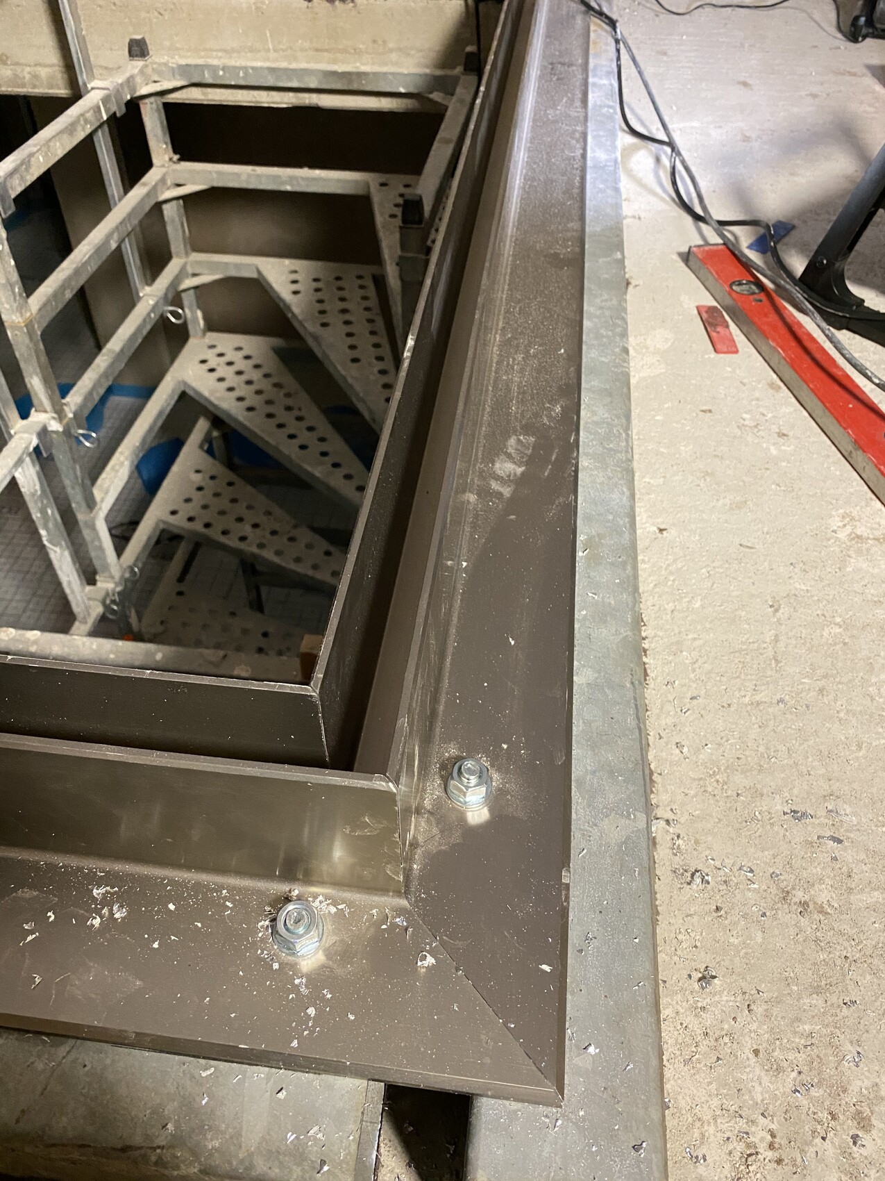 Sicht auf eine Stahlplattform mit Bolzen; linke Seite eine perforierte Stahltreppe im offenen Schacht.