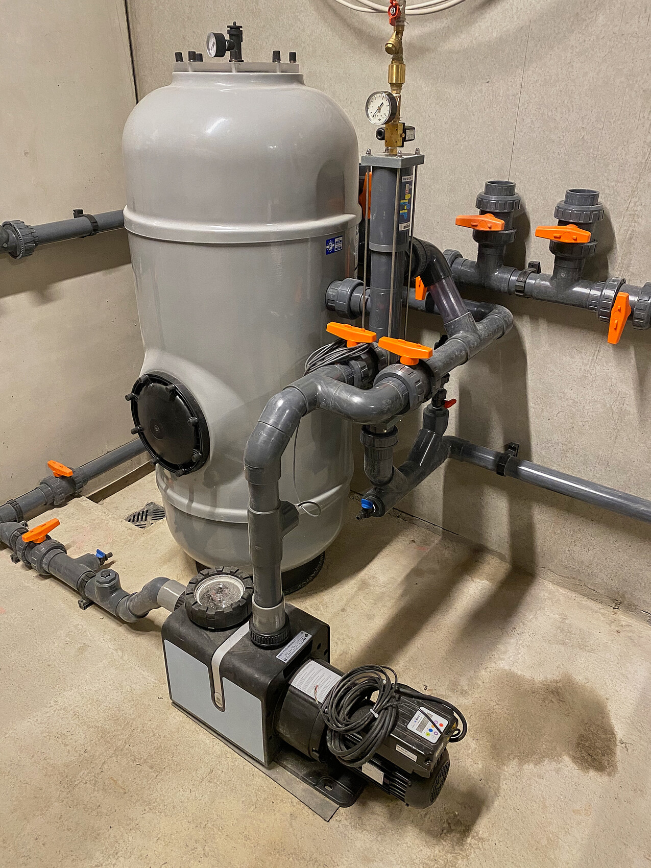 Großer grauer Filtertank mit Pumpe, Ventilen und Rohrleitungen im Technikraum