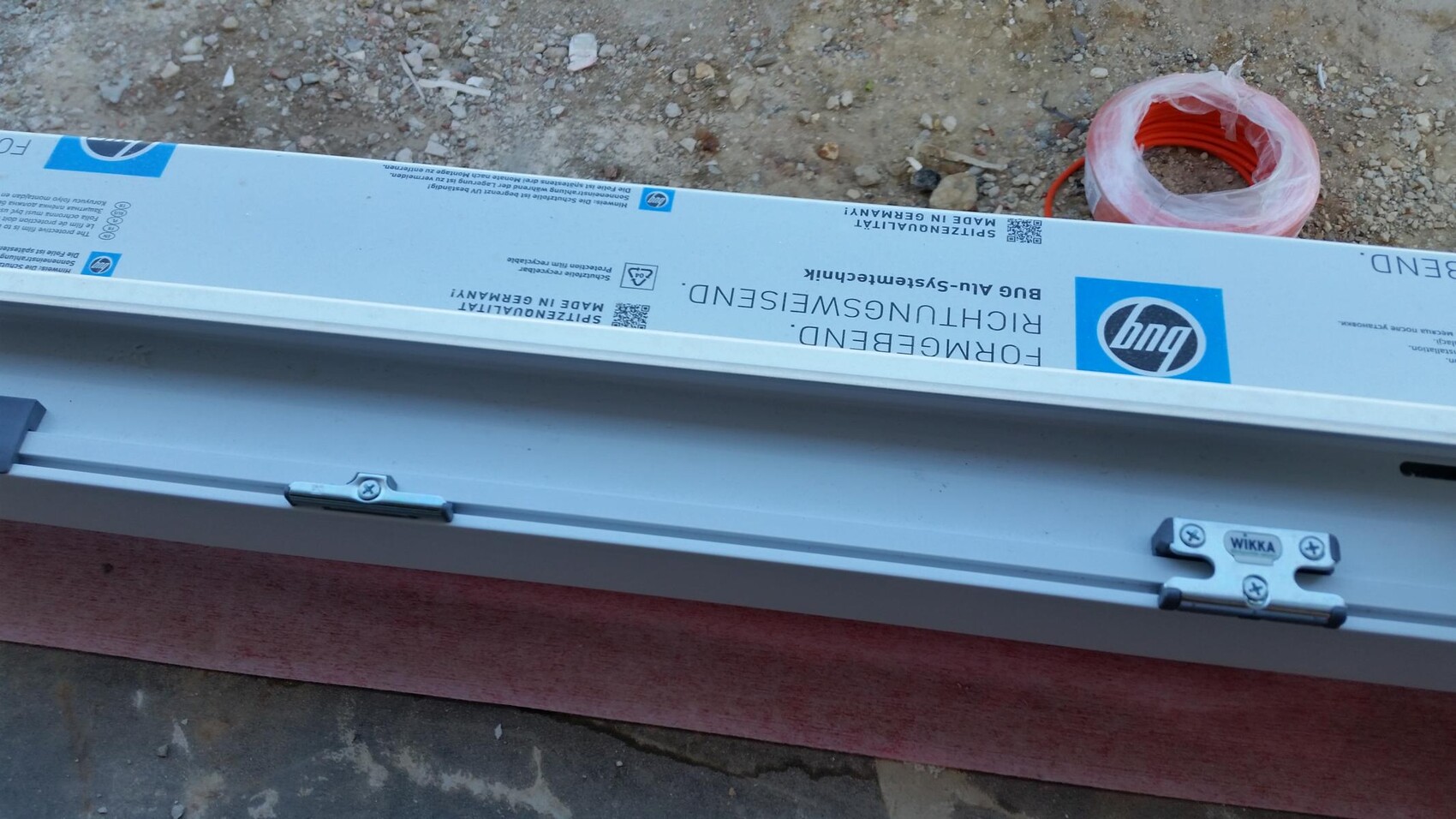 Langer Metallrahmen auf einer Baustelle mit WIKKA-Beschlag; daneben eine orange Kabelrolle.