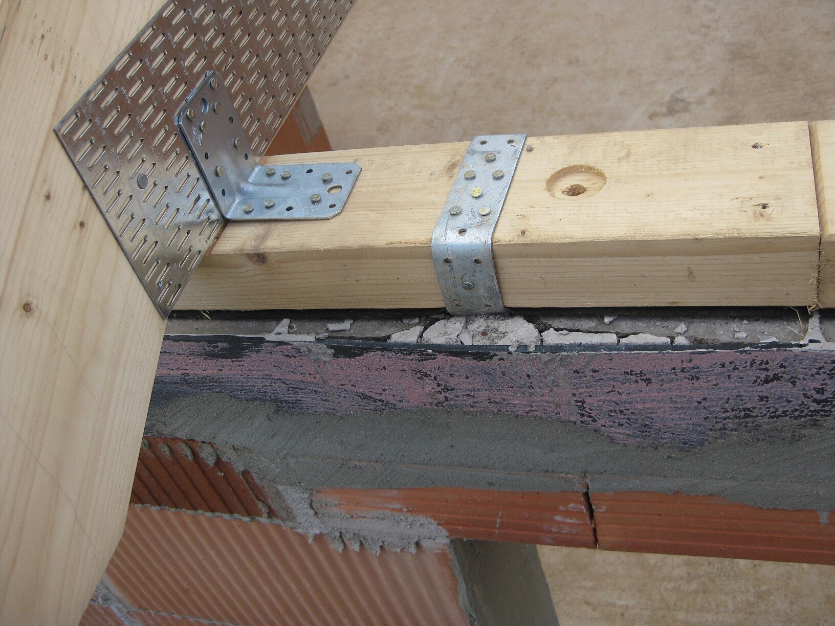 Holzbalken mit Metallwinkel-Verbindung an Holzbaukonstruktion über Ziegel- und Mörtelunterbau.