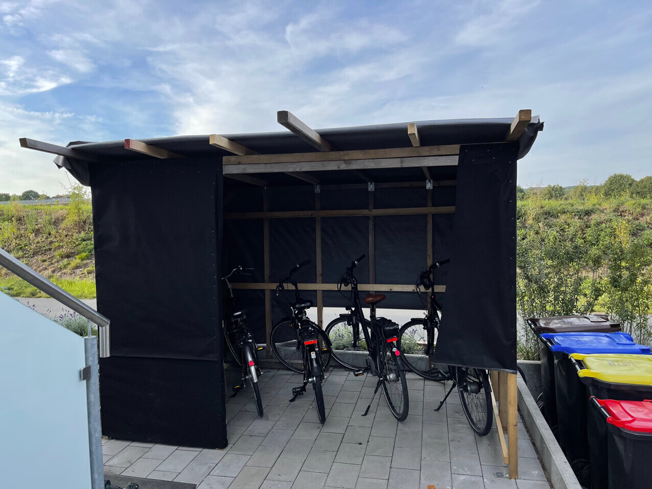 Fahrradschuppen aus schwarzem Stoff mit mehreren Fahrrädern auf gepflastertem Boden.