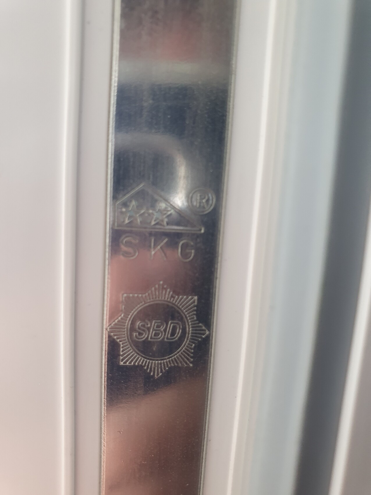 Nahaufnahme eines Metall-Tuerbeschlags mit SKG-, SBD- und R-Siegeln.