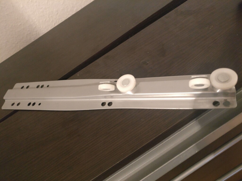 Metall-Schubladenführung mit weißen Rollen auf Holzunterlage.