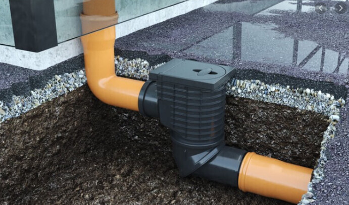 Freigelegter Graben: orange PVC-Rohre verbinden sich mit schwarzem Verbindungsstück und Deckel.