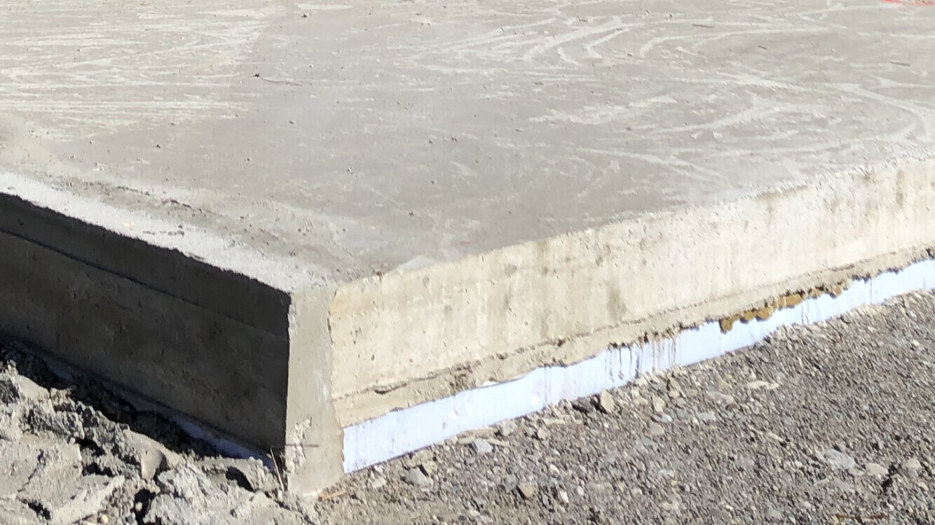 Betonplatte mit sichtbarer Dämm- oder Abdichtungsbahn an der Unterkante, Kiesboden daneben.
