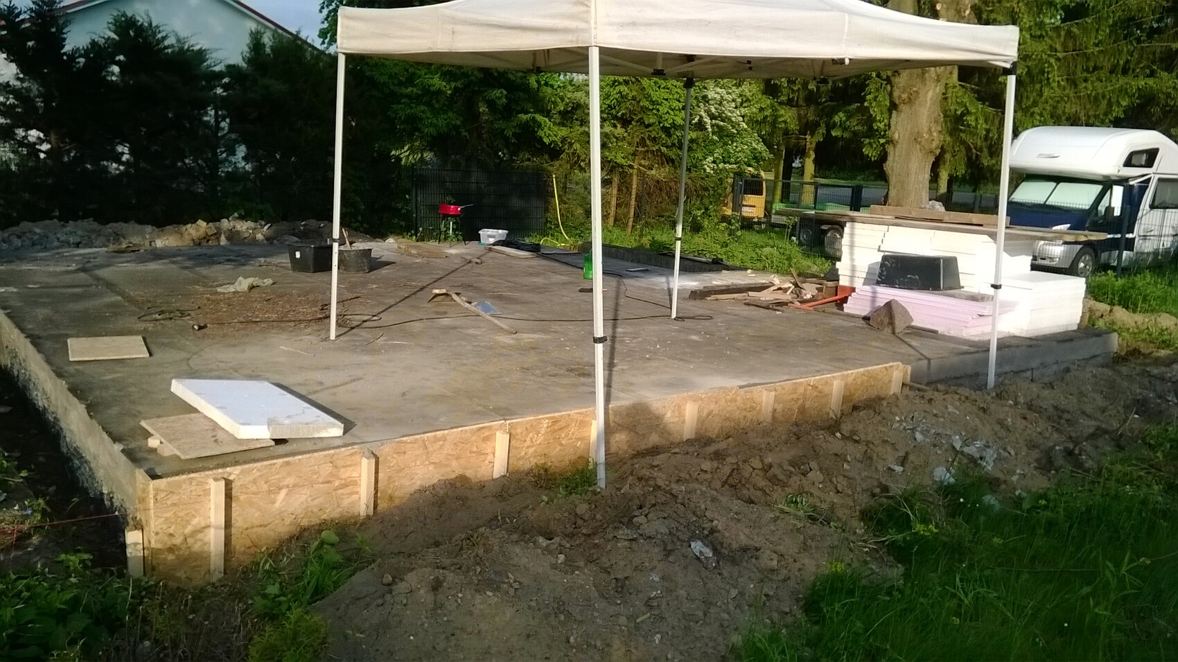 Große Betonplatte auf Fundament mit Zeltdach, Dämmplatten, Holz und Werkzeugen auf der Baustelle.