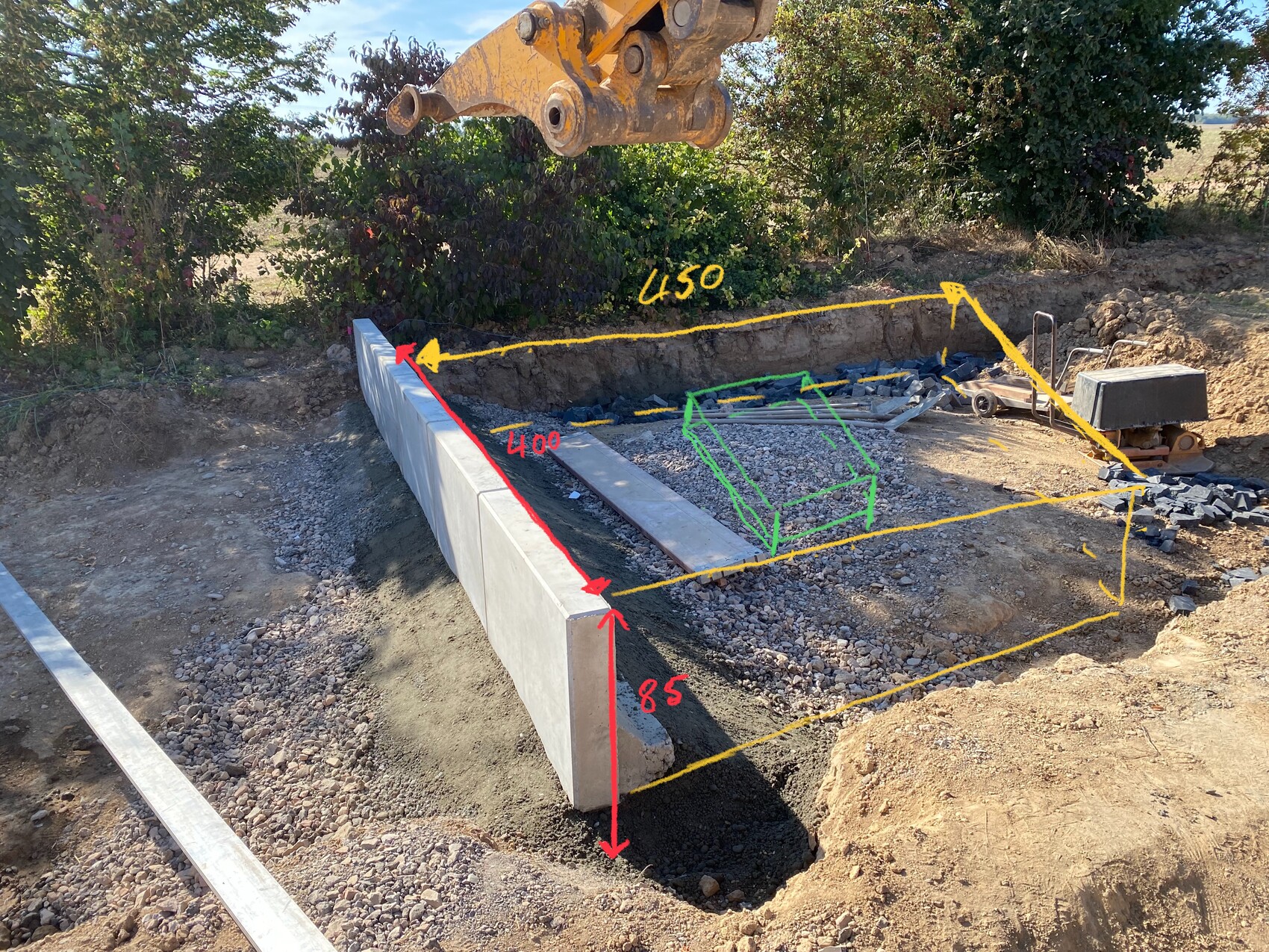Baustelle: langer Betonblock in Graben, gelbe Markierungen, grüner Würfel, Baggerarm darüber.