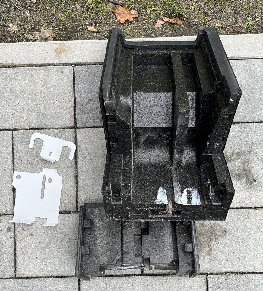 Schwarzer Kunststoffbehälter mit Innenfächern, daneben zwei weiße Metallhalter.