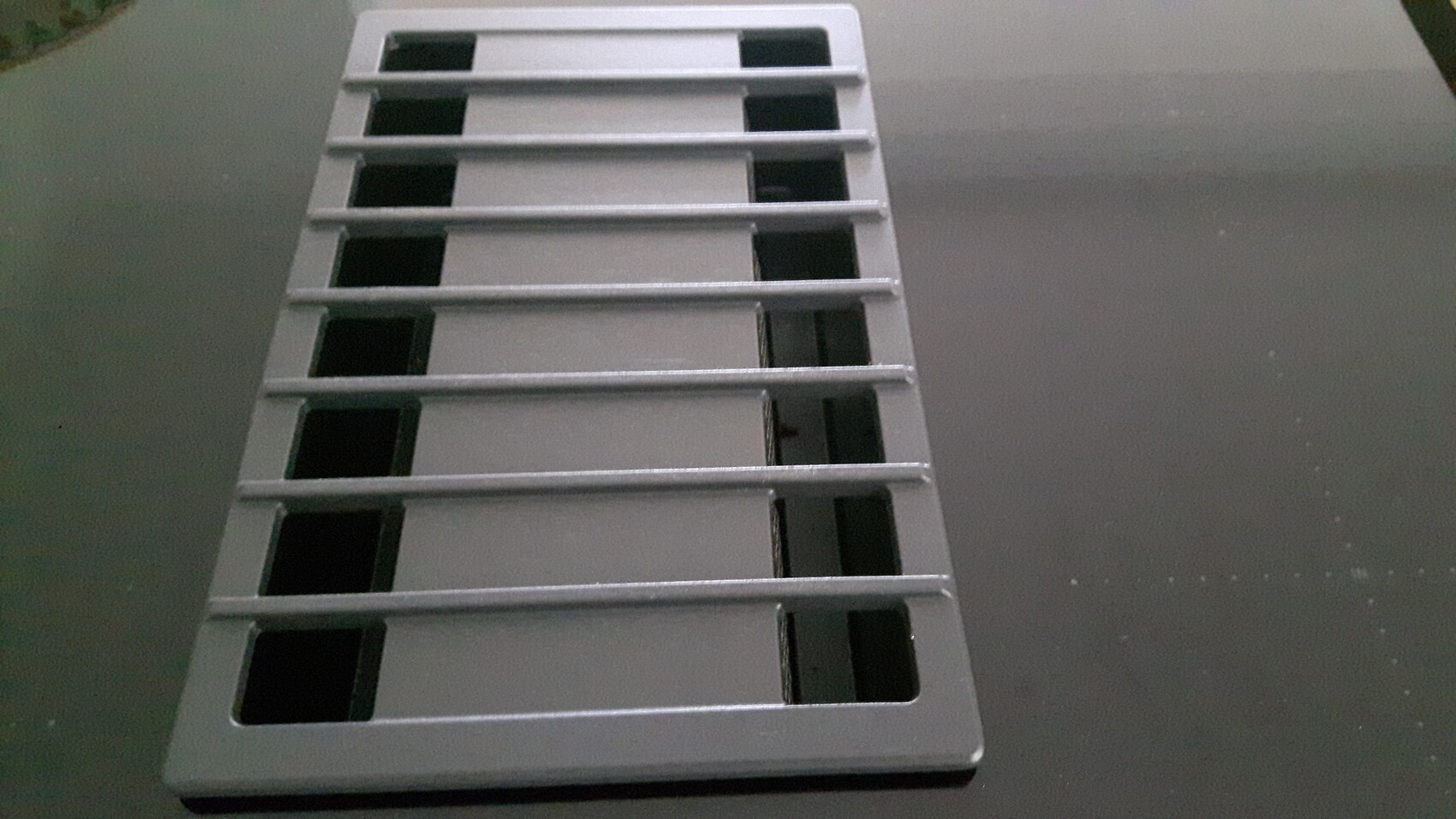 Metallisches Bodenabflussgitter mit parallelen rechteckigen Öffnungen auf grauem Untergrund