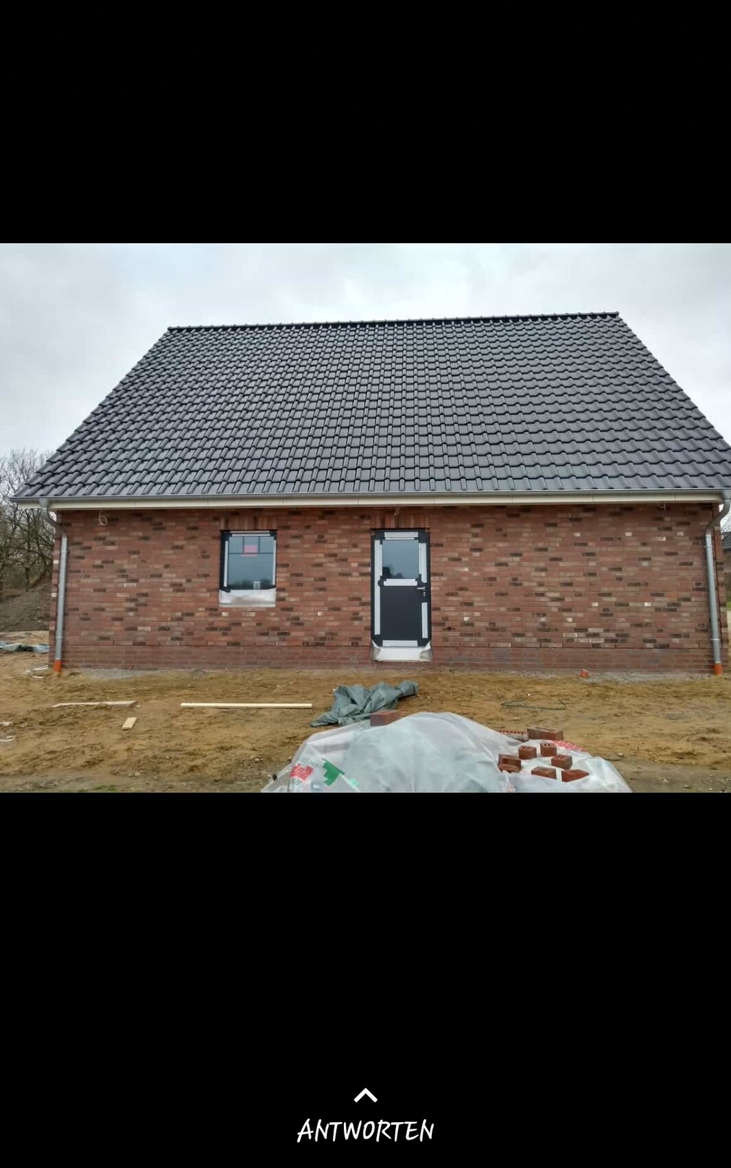 Neubau eines roten Backsteinhauses mit großem grauen Ziegeldach; Bauutensilien davor.