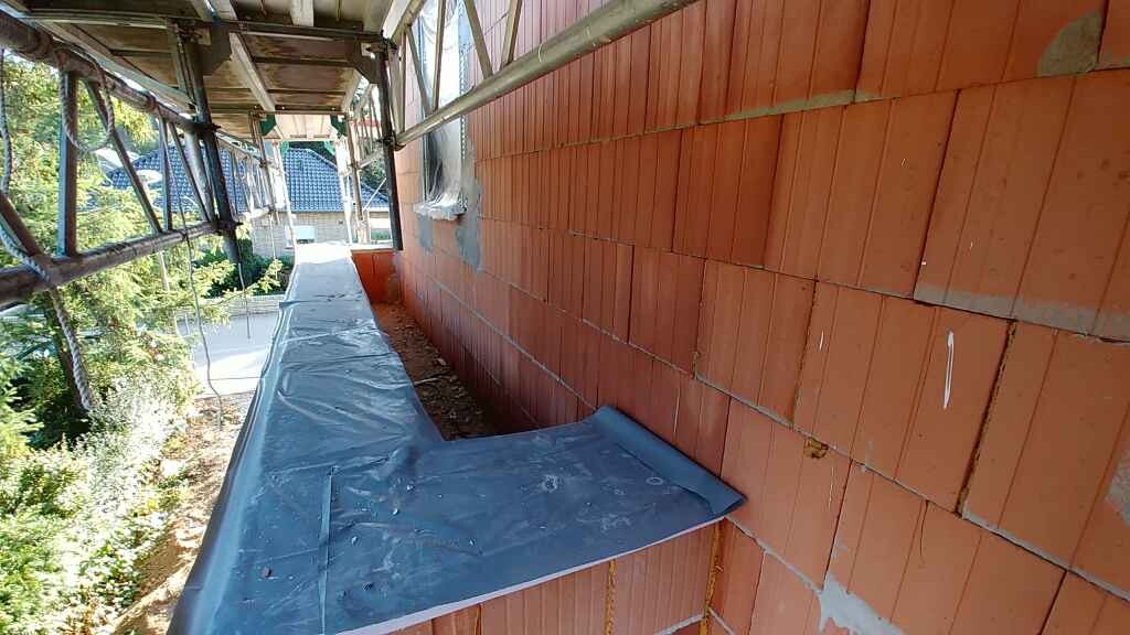 Aussenwand aus roten Ziegeln, Geruest und blauer Abdeckung an einer Baustelle