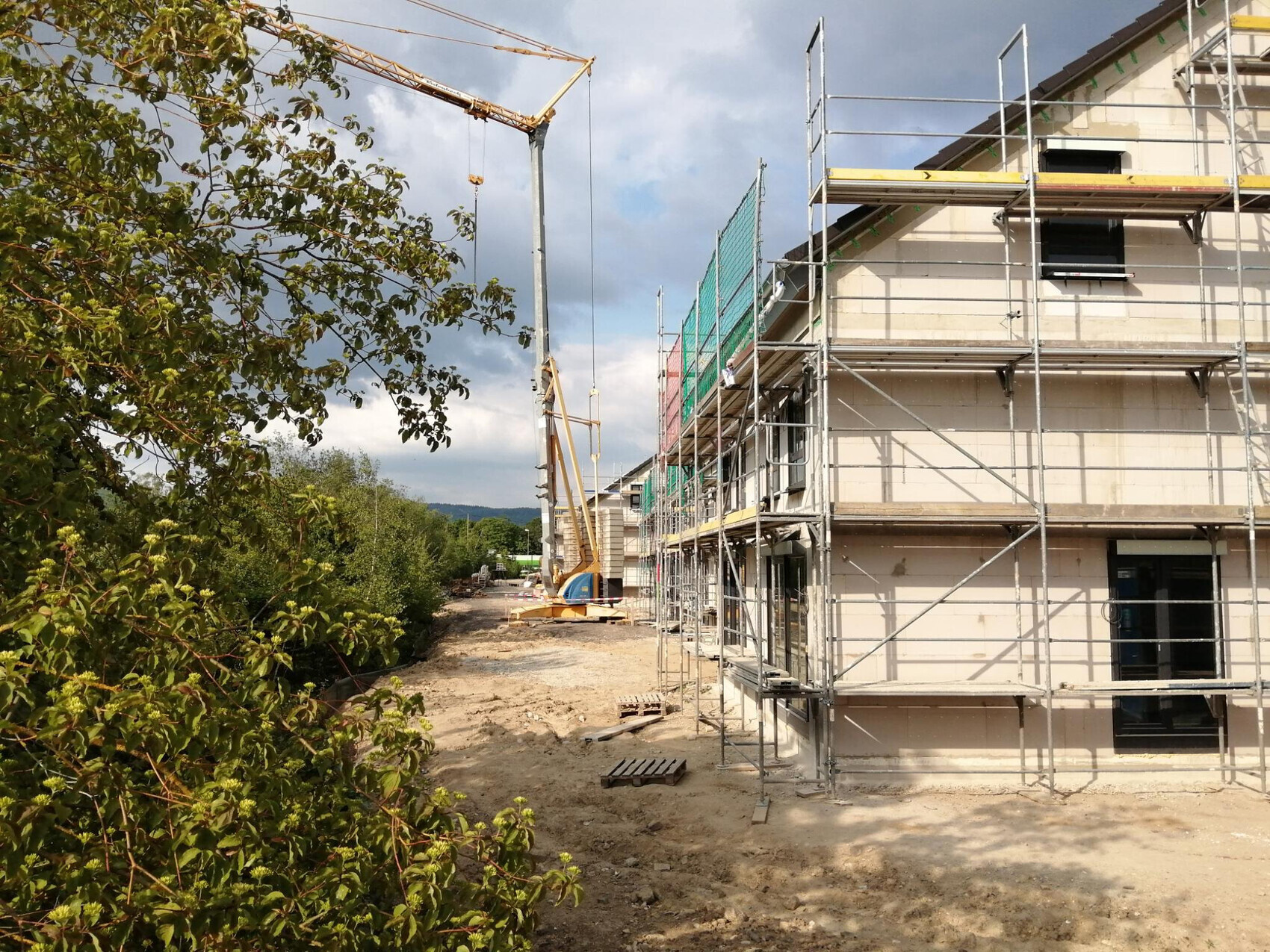 Baustelle mit Gerüst am Gebäudefront, Kran rechts, Erde und Bäume links.
