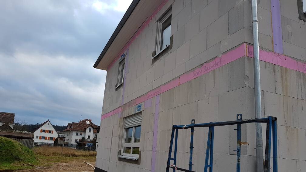 Neubauhaus mit pinken Dämmplatten, Fenstern und Baugerüst auf Baustelle