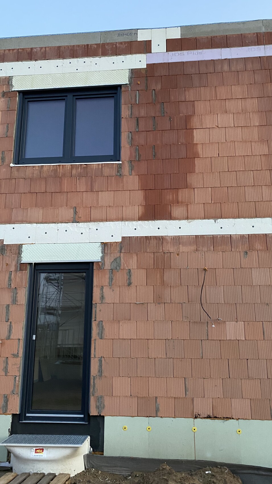 Ziegelbau-Fassade mit zwei dunkel gerahmten Fenstern, Bauarbeiten sichtbar