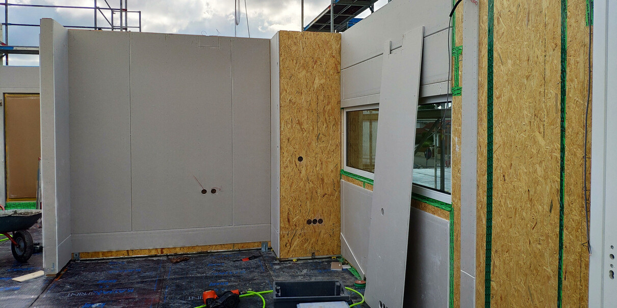 Baustelle mit Rohbauwand aus OSB-Platten, Fensterrahmen und Baumaterialien sichtbar