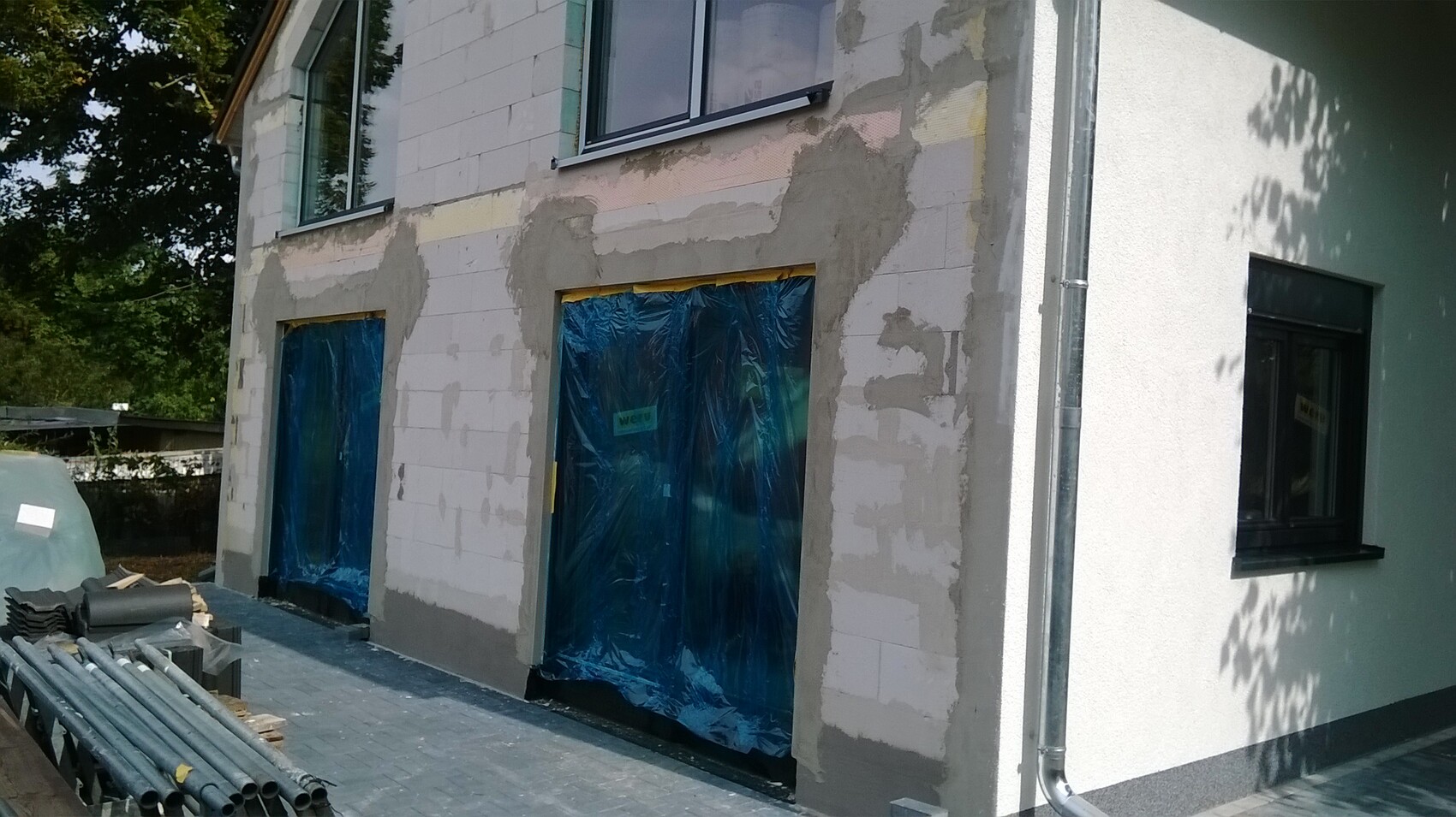 Außenfassade eines Hauses im Umbau; Türen und Fenster mit blauem Kunststoff abgedeckt.