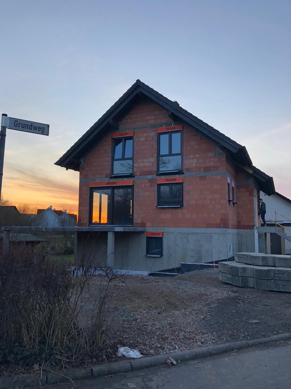 Zweistöckiges Ziegelhaus im Bau mit Betonfundament; Sonnenuntergang spiegelt sich im Fenster.