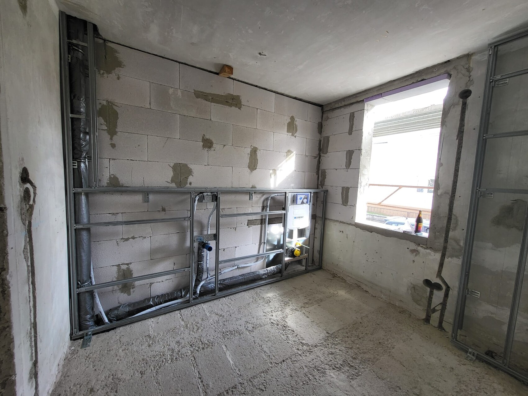 Baustelle: Innenraum mit Metallständerwerk, isolierten Rohren und offener Fensteröffnung.