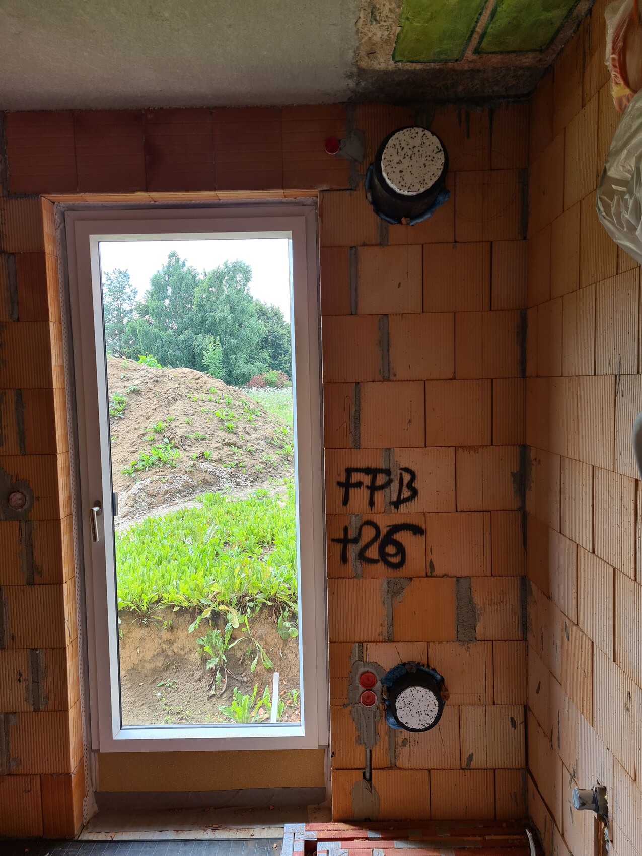 Unfertiger Badezimmer-Rohbau mit Wandsteinen, Installationen und Fensteraussicht