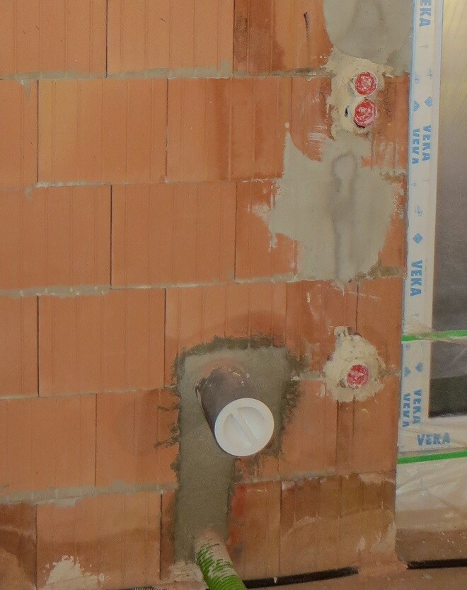 Unterbau aus roten Ziegeln, zentrales weißes Rohr mit Abdeckung, grüne Schlauchleitung unten.