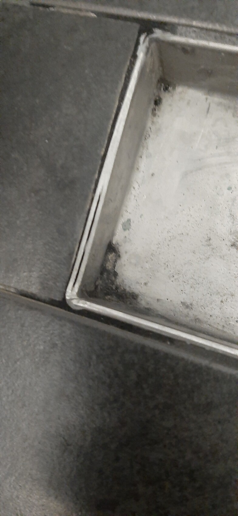 Nahaufnahme eines flachen Metallbehälters mit weißem Pulverstaub in der Ecke.