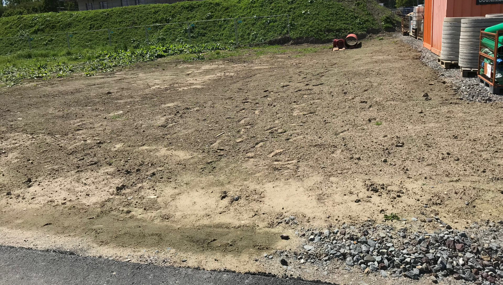 Unbefestigte Erdfläche mit Kies; rechts Lagerbereich mit orange Container und Baumaterialien