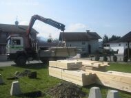 Bauplatz mit Kranbagger, Holzbauteile und Vorbereitungen für den Rohbau
