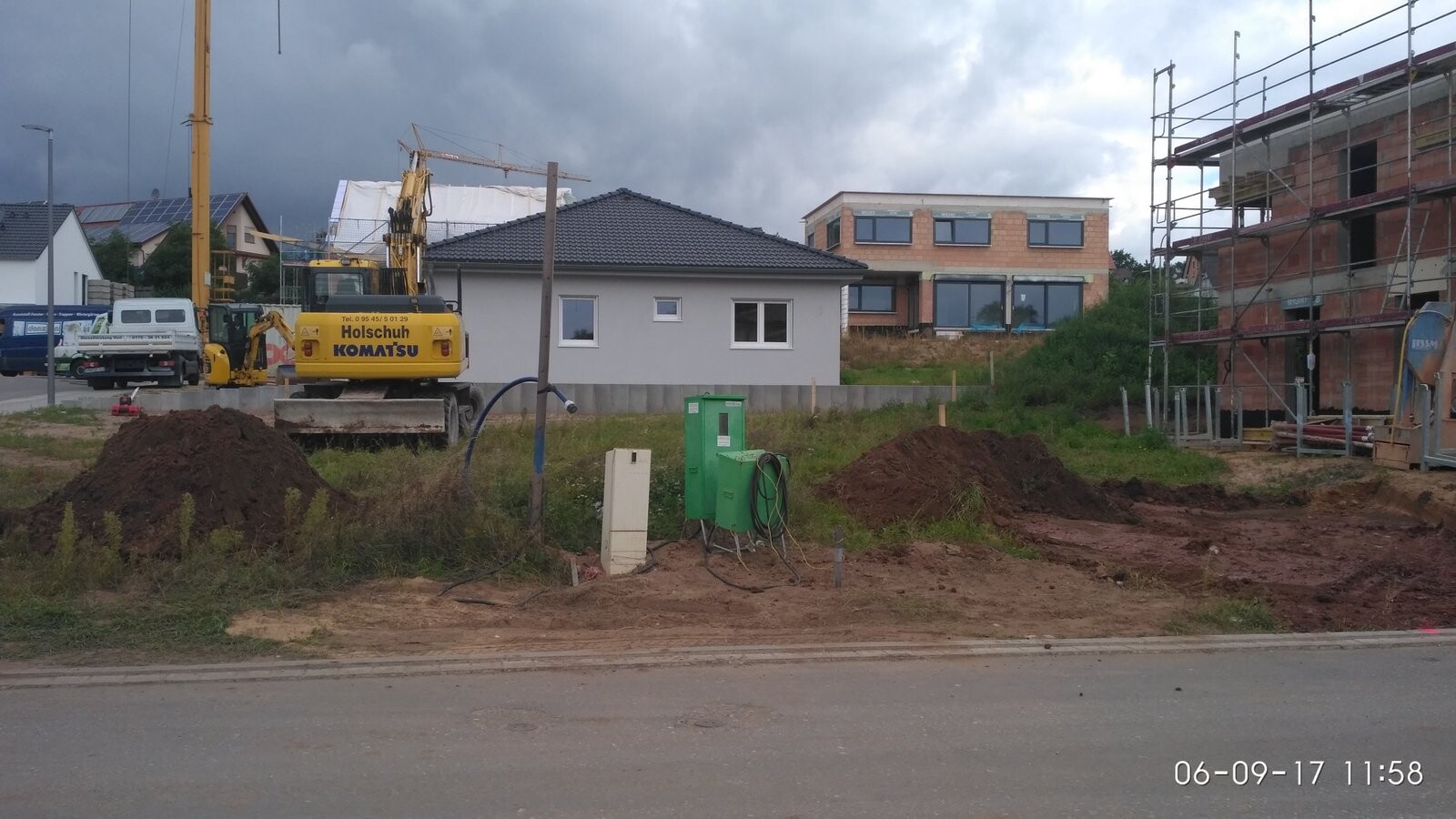 Baustelle mit Kran, Erdhaufen und Gerüsten; im Hintergrund fertige Häuser