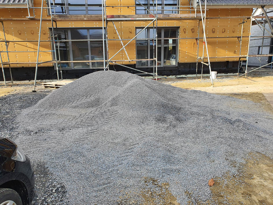 Baustelle: Gerüst um ein Gebäude, vorne ein großer Kieshaufen.