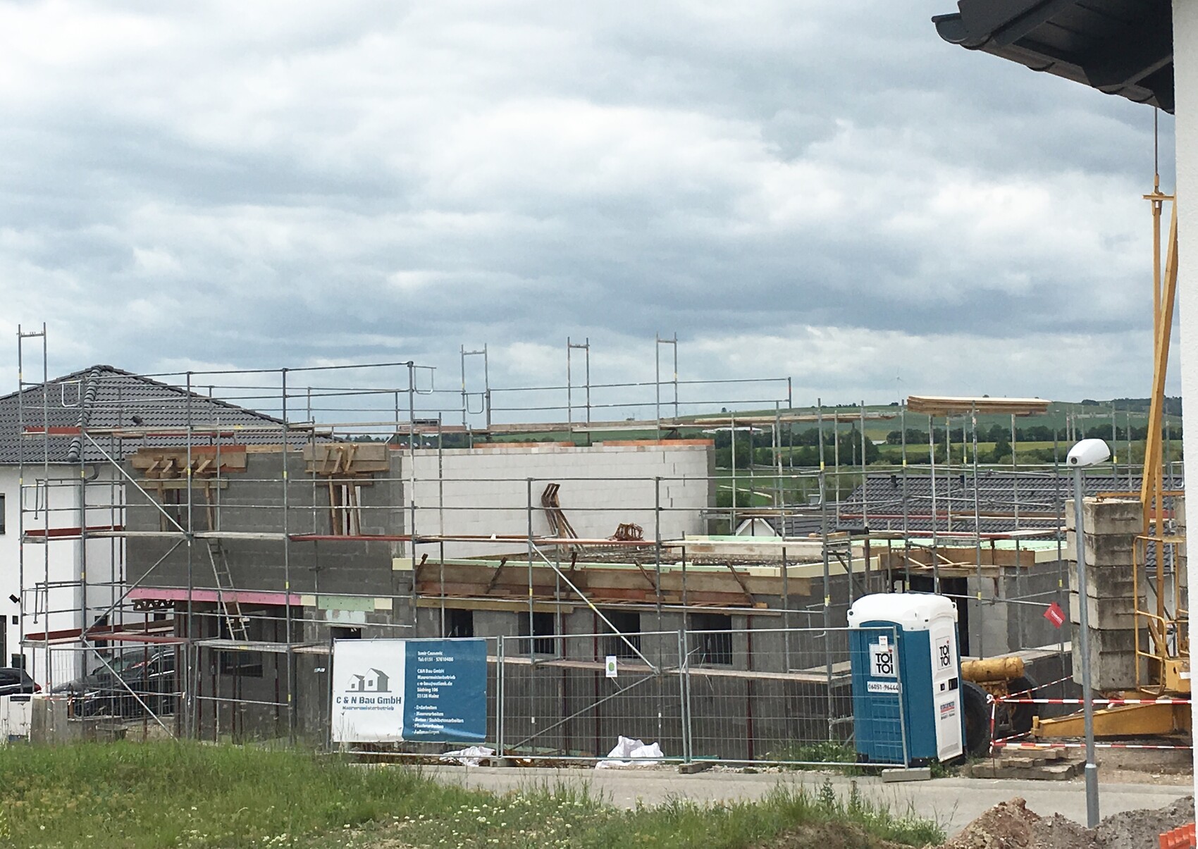 Baustelle mit Metallgerüst um Rohbau; Holzformarbeiten, Porta-Potty und Absperrband.