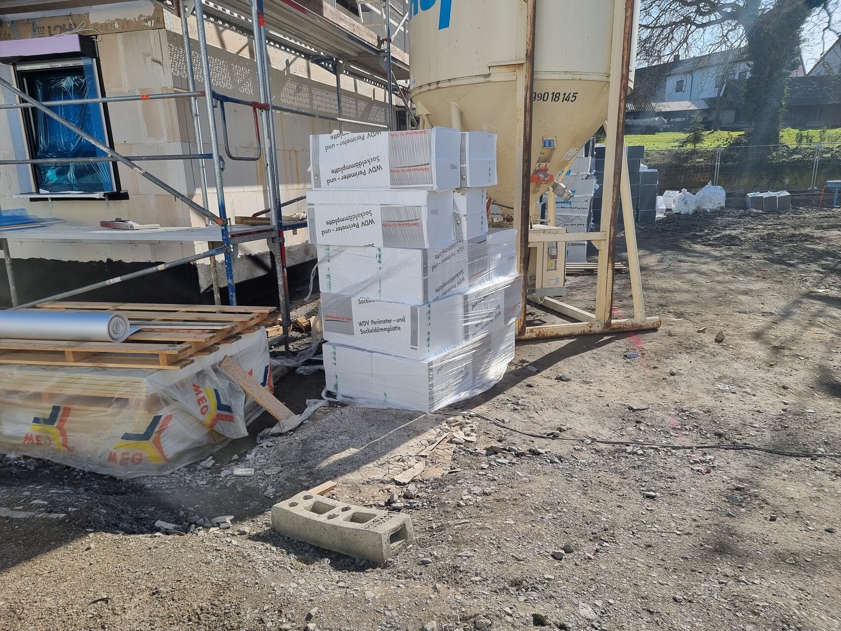 Baustelle mit Gerüst, Betonmischer, gestapelten Dämmplatten und Baumaterialien.