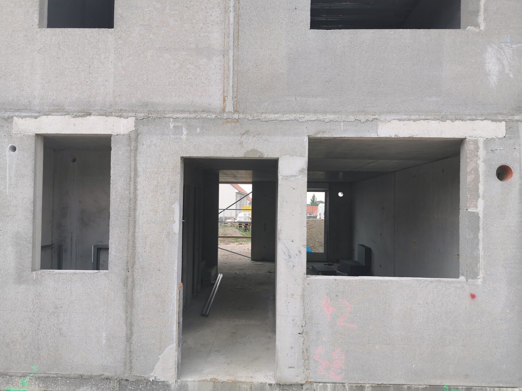 Rohbau aus Beton mit offenen Türen und Fensteröffnungen, Innenraum durch Türöffnung sichtbar.