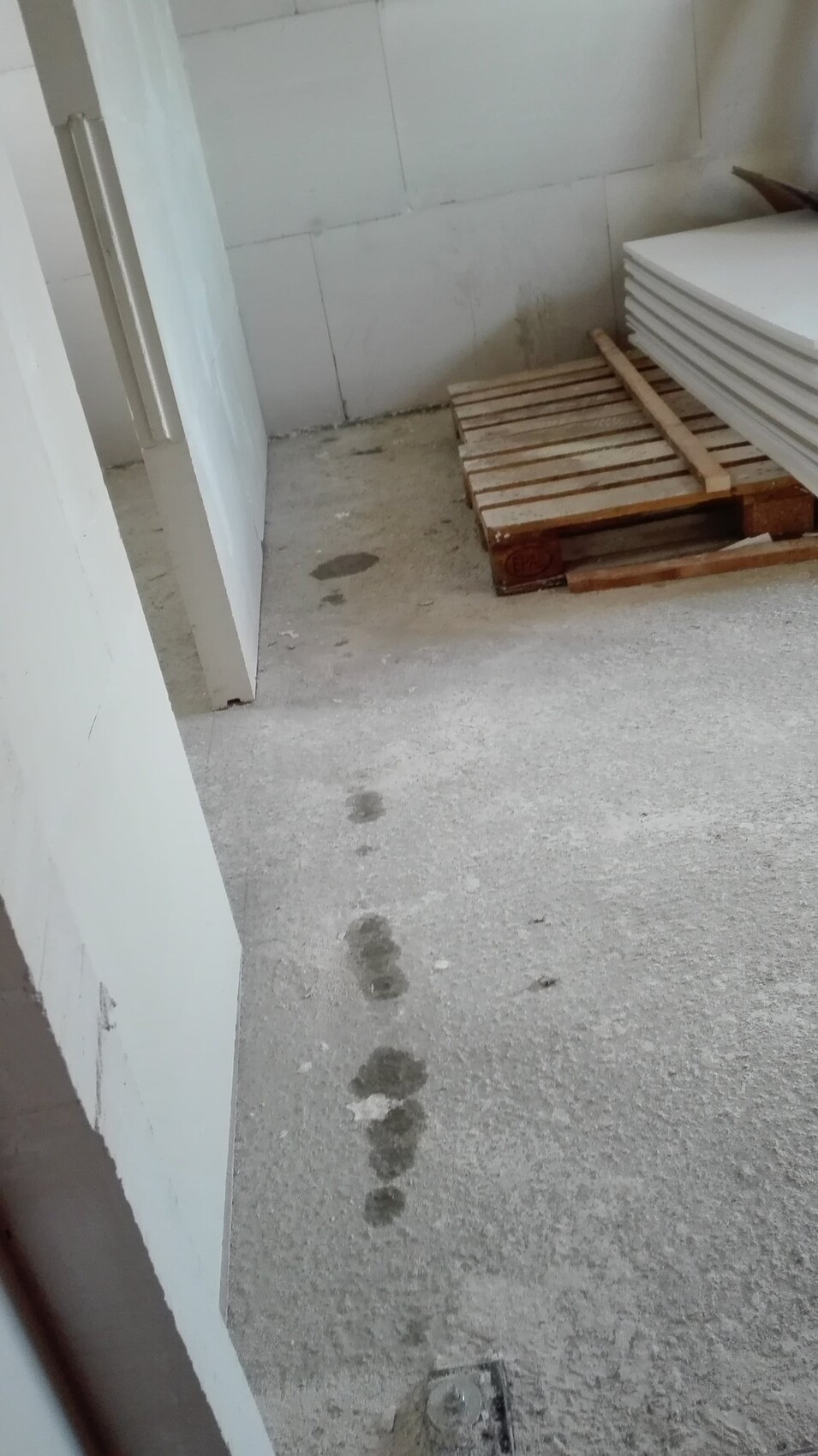 Rohbau-Baustelle: Betonboden, Holzpaletten und Baumaterialien stapelbereit