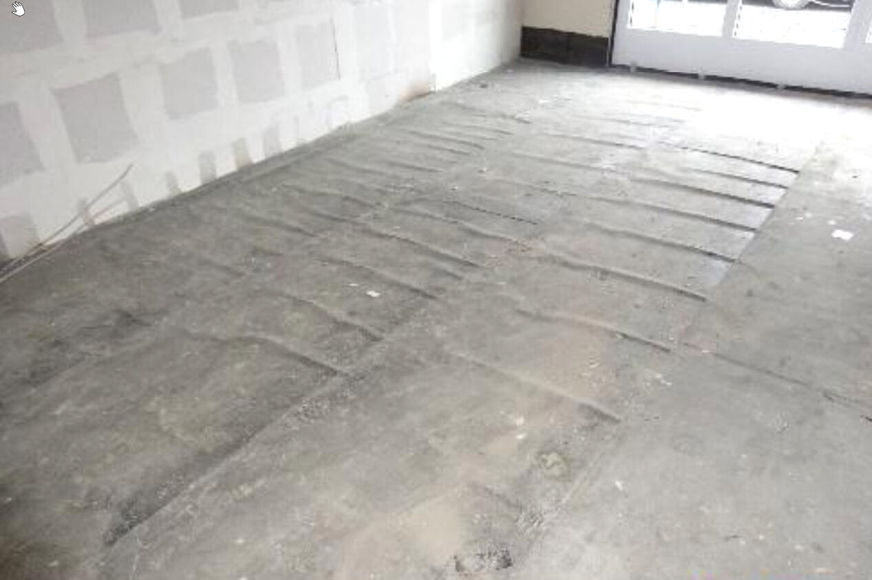 Renovierungsraum mit grobem Betonboden, gespachtelten Wänden und Tür am Ende.