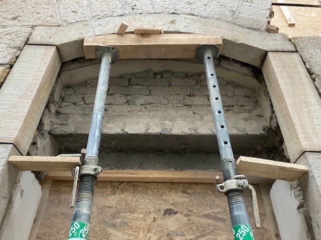 Baustellen-Gerüst mit Metallstützen und Holzbohlen vor einem Steinbogen